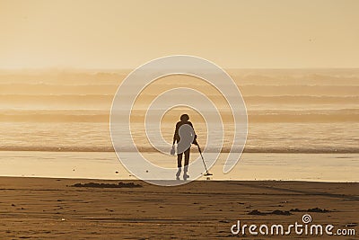 Using a metal detector to search for hidden treasure on a beach at sunset Editorial Stock Photo