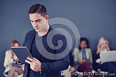 Using technology to achieve success. a handsome young businessman using a tablet with his colleagues in the background. Stock Photo