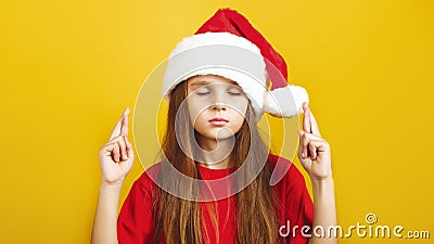 Ð¡ute little girl wearing Christmas Santa hat make a wish standing isolated over yellow background Stock Photo
