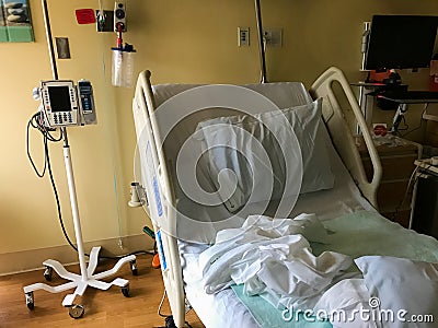 Vacant rumpled hospital bed with IV pole nearby Stock Photo