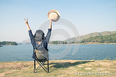 Asian woman wear hat and sitting relax on portable chair nearly lake at National Park. Stock Photo