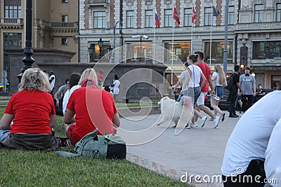 Family with a white fluffy dog walks amicably down the street in step on the Manege square in Moscow Editorial Stock Photo