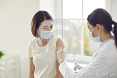 Young woman in a protective face mask getting an antiviral vaccine at the clinic Stock Photo