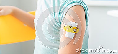 Vaccination of little girl in doctor`s office.Kids funny adhesive plaster,gauze napkin.Sits on chair.Vaccine for covid-19 Stock Photo