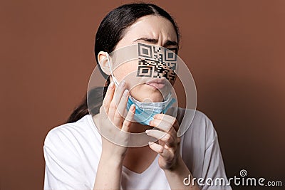 Vaccination. Portrait of a woman with a QR code instead of eyes and nose, examining her new face. Brown background. The Stock Photo