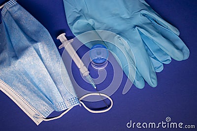 Vaccine bottle phial with no label, medical syringe with injection needle, blue medical mask and gloves . isolated on blue Stock Photo