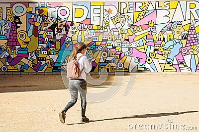 Valencia, Spain - December 21, 2019: Young girl walks in front of an artistic mural while listening to music through her Editorial Stock Photo