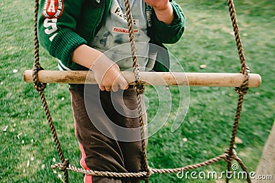 Valencia, Spain - January 30, 2017: Child perched on a wooden ladder hanging from a tree, enjoying childhood games outdoors in Editorial Stock Photo