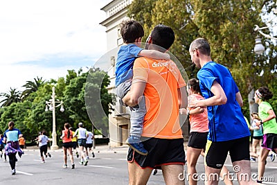 Valencia, Spain - May 19, 2019: Father carrying in his arms his son who participates in a popular running race Editorial Stock Photo