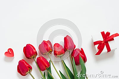 Valentine Day Romantic Background. Red tulips, a gift with a bow, and candle hearts on a white background with copying space. Flat Stock Photo