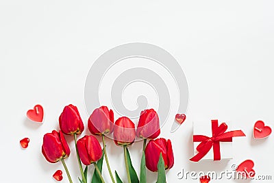 Valentine Day Romantic Background. Red tulips, a gift with a bow, and candle hearts on a white background with copying space. Flat Stock Photo