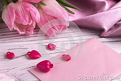 Valentine`s day background with pink tulip flowers red hearts shape sign on white pink envelope on white wooden background. Stock Photo