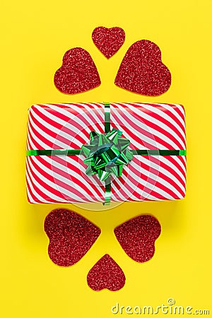 Valentines Day card. Wrapped gift. Minimalistic design. Festive present and red hearts on a yellow paper background, romantic Stock Photo