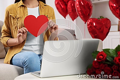 Valentine's day celebration in long distance relationship. Woman holding red paper heart while having video chat with her Stock Photo