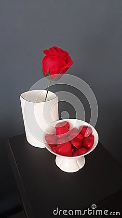 Valentine`s Day, red rose in a white vase, lots of hearts in a white vase, gray on a black background. Stock Photo