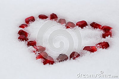 Valentine`s heart shape made by pomegranate seeds on white snow. Stock Photo