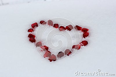 Valentine`s heart shape made by pomegranate seeds on white snow. Stock Photo