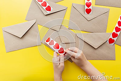 Valentine's day. Hands glue red hearts on envelopes, yellow background. The holiday is February 14. Love letters Stock Photo