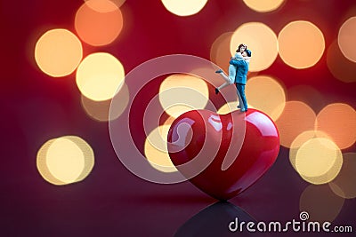 Valentines card or wallpaper with sweet miniature couple standing on red heart shape with red background and beautiful bokeh Stock Photo