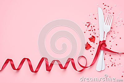 Valentines day background or concept for lunch menu. Cutlery white fork and knife entwined with red ribbon and small hearts on Stock Photo
