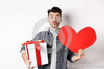 Valentines day and love concept. Guy waiting for kiss, bring lovely gifts and red heart card, pucker lips and look at Stock Photo