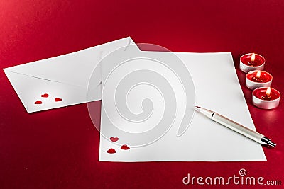 Valentines love letter writing setup, with envelope, paper, red hearts and candles with fire and flame on a red background. Stock Photo
