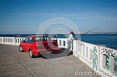 Man with fishing rod is fishing on seafront of Valparaiso city. Red Daewoo car is parked on embankment Editorial Stock Photo