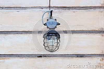 vandal-proof round street lamp hanging on a beige background of old plaster wall. Stock Photo