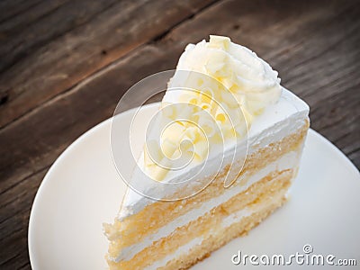 Vanilla sponge cake with cream and white chocolate decorate. Sliced piece of cake on white plate. Served on wooden table. Stock Photo