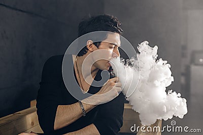 Vaping man holding a mod. A cloud of vapor. Black background. Stock Photo