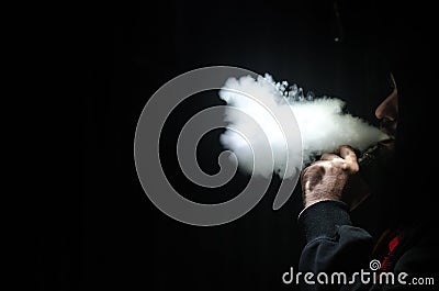 Vaping man holding a mod. A cloud of vapor. Black background. Vaping an electronic cigarette with a lot of smoke Stock Photo