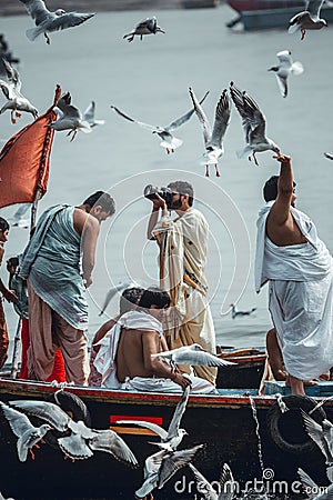 Varanasi, India, 16 november, 2019 / Boat passing on the Ganges with curious persons on top; a fat man in white feeding the birds, Editorial Stock Photo