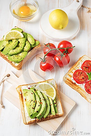 Variation of healthy breakfast toasts with avocado and cherry tomatoes on white wooden background. Food concept Stock Photo