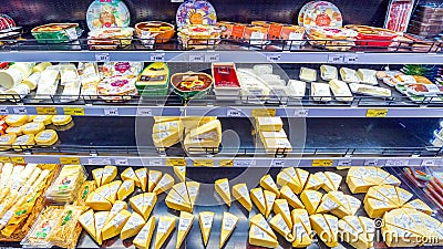 a variety of cheeses in the refrigerated display case In a large supermarket. Editorial Stock Photo