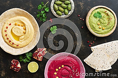A variety of colored hummus, pita bread, olives, pomegranate on a dark woody background. Top view, place for text. Stock Photo