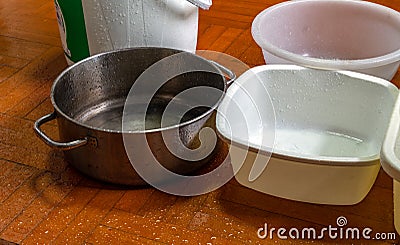 Variety of containers arranged on the wooden floor of house. To accommodate rainwater leaking from the roof while in heavy rain Stock Photo