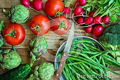 Variety of fresh colorful organic vegetables green beans, tomatoes, red radish, artichokes, cucumbers on wood kitchen table, copy Stock Photo