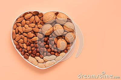A variety of nuts in a bowl a heart shape on a pink pastel background. Almonds, walnuts, hazelnuts, peanuts. Top view, flat lay, Stock Photo