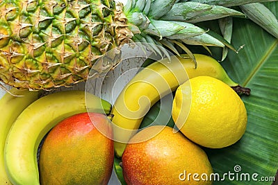 Variety of Tropical Fruits Pineapple Mango Bananas Lemons Green Palm Leaf on White Planked Wood Stock Photo