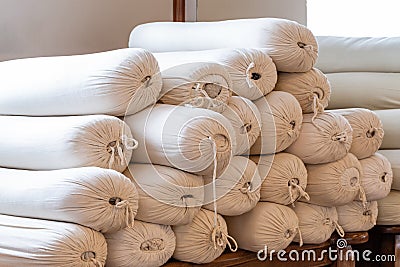 White rolled mats, cork brick, belt, grey bolster and folded cotton mat. Variety of yoga props on wooden floor in studio Stock Photo