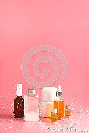 Various bottles, jars and containers with cosmetics on pink with splashing waters. Stock Photo