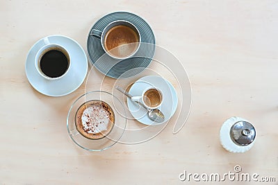 Various coffee drinks like espresso, cappuccino, lungo black and with crema and a sugar dispenser on a light wooden table, Stock Photo