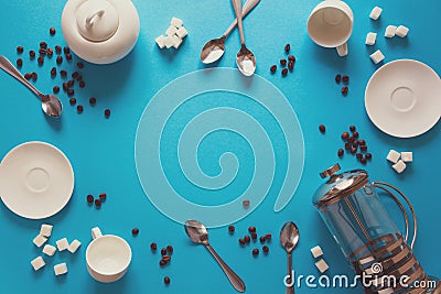 Various coffee making accessories: French coffee press, cups, saucers, coffee beans, spoons and sugar on blue paper background. Stock Photo