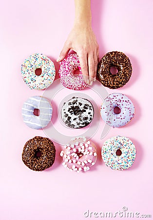 Various donuts on a pink background. A woman`s hand taking one. Stock Photo