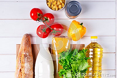 Various healthy food, tomato, bread, pasta, pepper, oil and vegetables in paper bag on white wooden background. Food Stock Photo