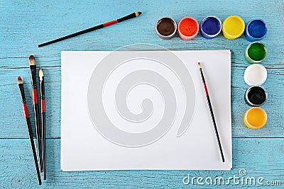 Various paints, brushes, white sheets paper on wooden blue background. Top view. Stock Photo