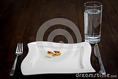 Various pills are on white plates next to a glass of water on a brown table Stock Photo