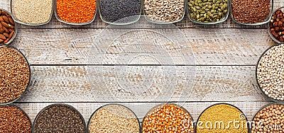 Various seeds and grains in bowls frame an old wooden board table - top view Stock Photo