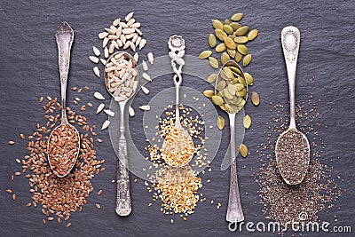 Various seeds - sesame, flax seed, sunflower seeds, pumpkin seed, chia in spoons on black background. Top view Stock Photo