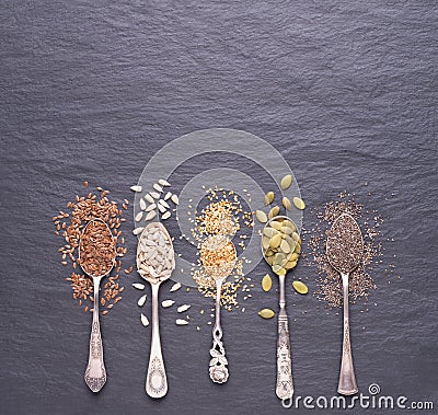 Various seeds - sesame, flax seed, sunflower seeds, pumpkin seed, chia in spoons on a black stone background. Top view Stock Photo